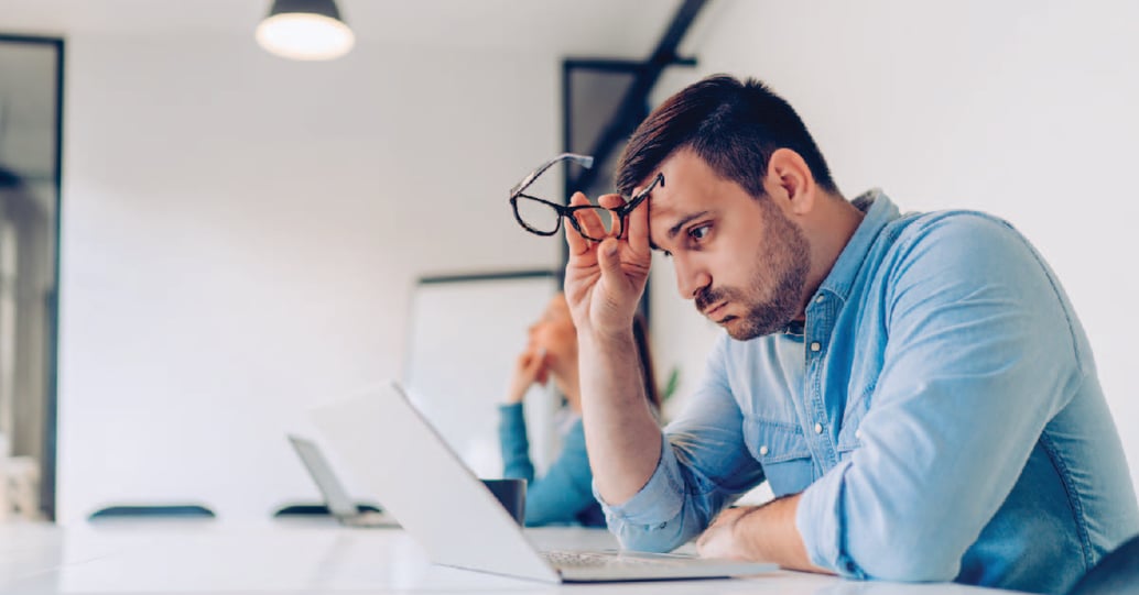 A male employee appears very stressed as he reviews information on a laptop at work.