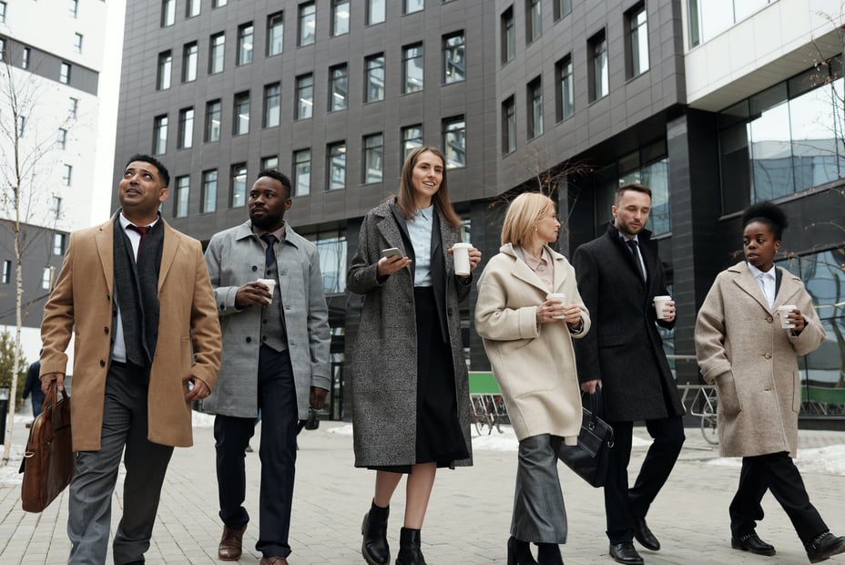 A diverse group of corporate employees take a walk together while drinking coffee.