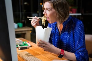 Businesswoman eating noodles at her desk in the office