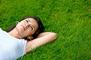 Pensive woman lying on grass listening to music outdoors