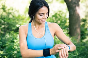 Smiling sporty woman in headphones using smart watch outdoors in park-1