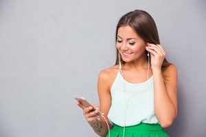 Smiling young girl listening music on smartphone over gray background