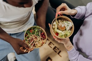 two people eating bowl of food with chopsticks