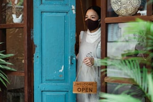 woman in mask holding open sign